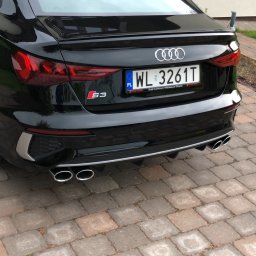 AS-TJ SPÓŁKA Z OGRANICZONĄ ODPOWIEDZIALNOŚCIĄ - Czarny samochód Audi S3 z widocznym tyłem, tablicą rejestracyjną WL 3261T, czterema chromowanymi końcówkami wydechu i logo S3, stojący na kostce brukowej.