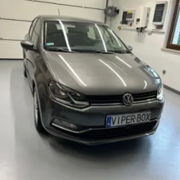 Szary Volkswagen Polo po umyciu, stojący w czystym garażu z białą bramą segmentową i instalacją elektryczną na ścianie.