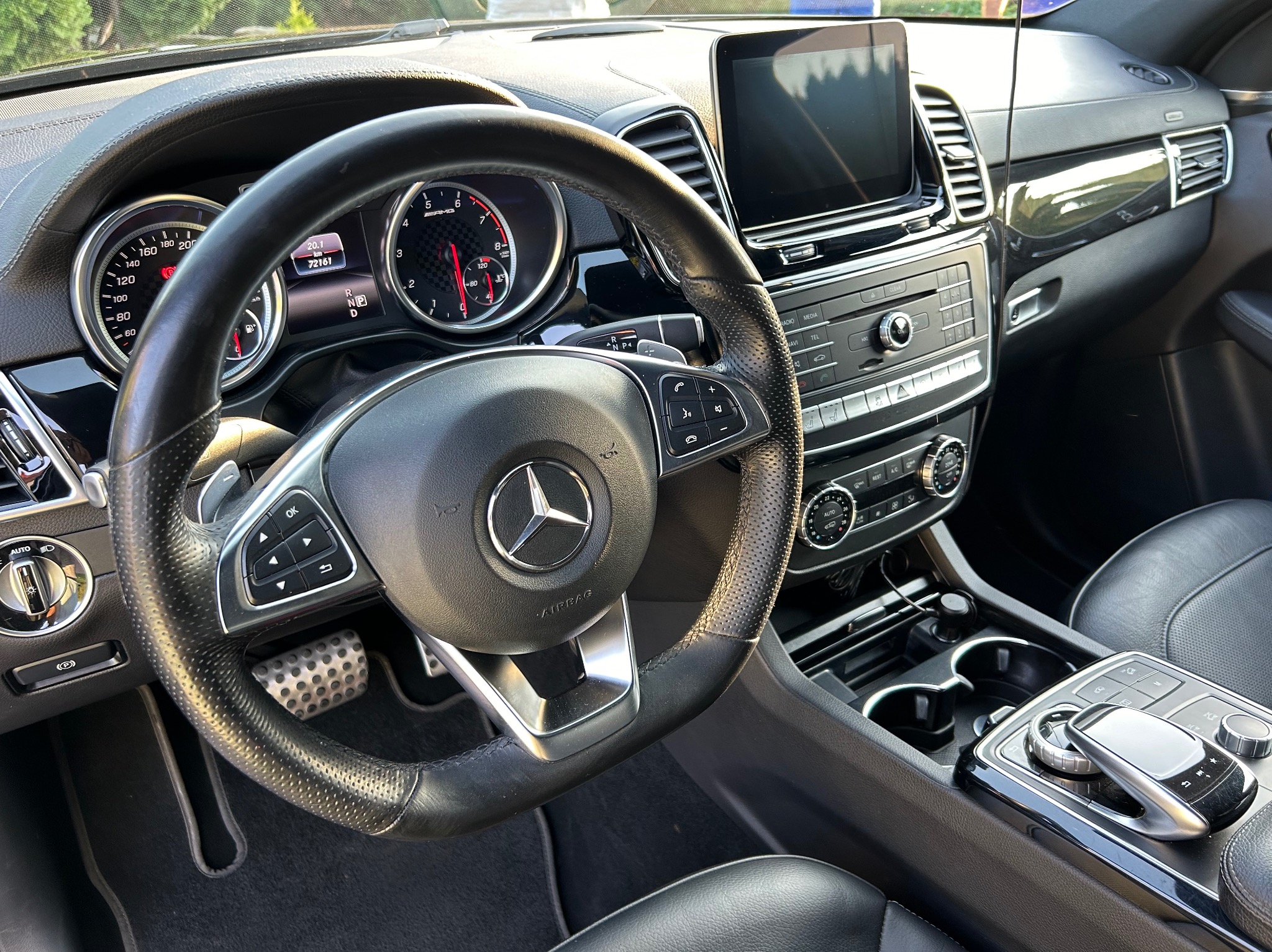 Wnętrze samochodu Mercedes-Benz GLE z widoczną deską rozdzielczą, kierownicą z logo i ekranem nawigacji. Widoczne czarne skórzane fotele i elementy wykończenia.