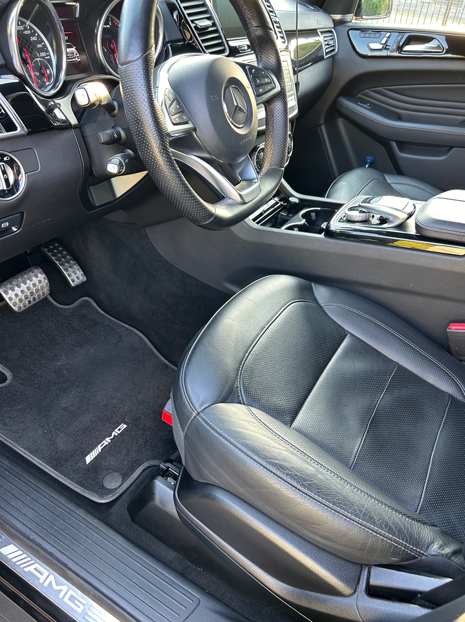 Wnętrze samochodu Mercedes-Benz AMG z czarną skórzaną tapicerką, widoczny fotel kierowcy, dywaniki z logo AMG i elementy deski rozdzielczej.