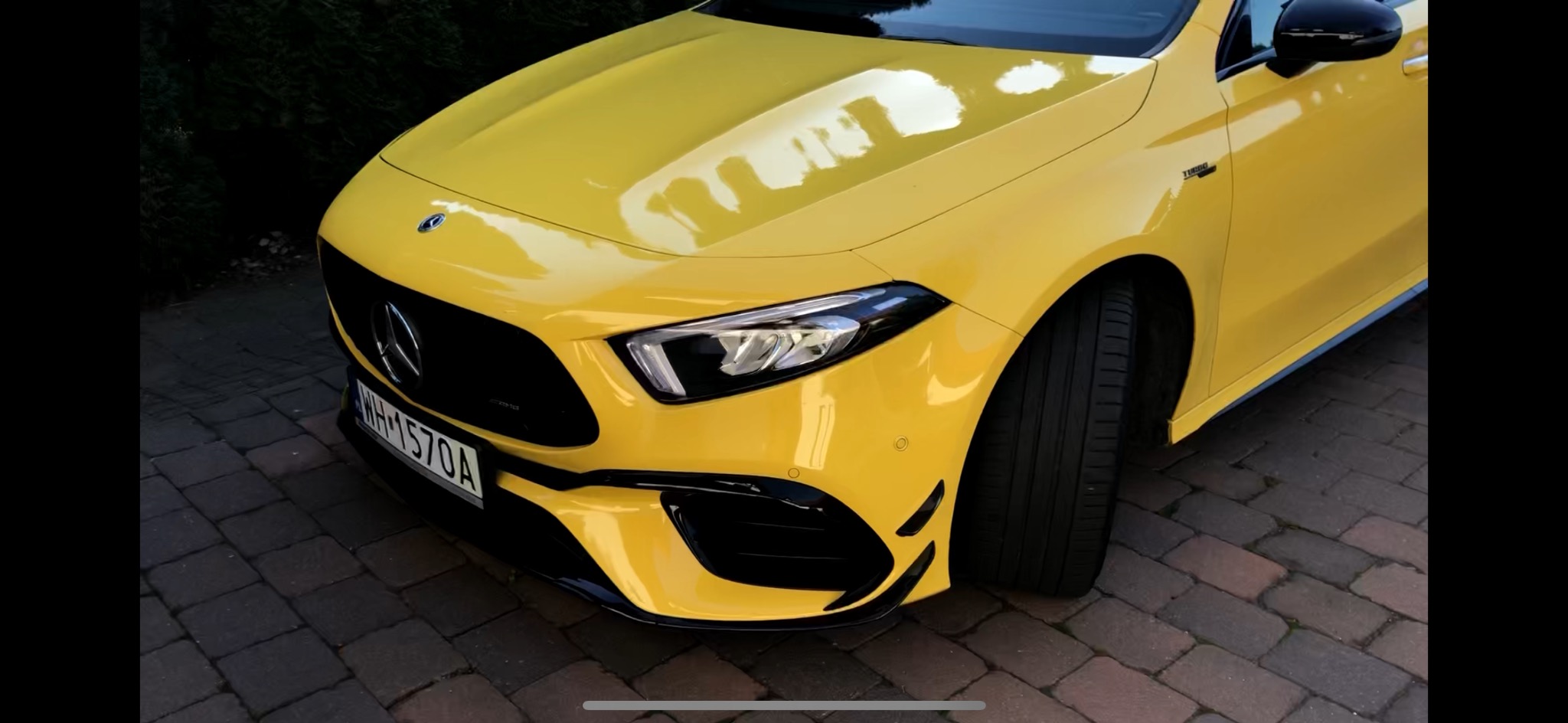 Żółty Mercedes-Benz klasy A AMG z czarnymi akcentami, widok z przodu na kostce brukowej.