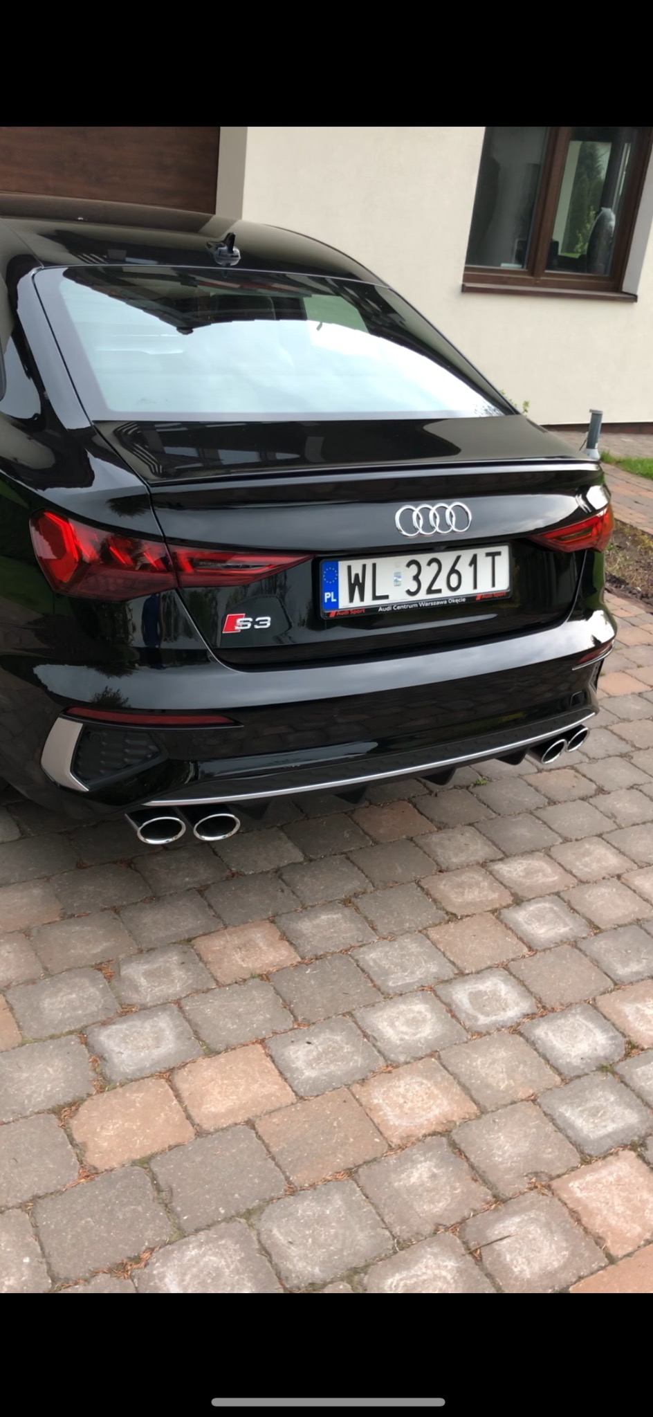 Czarny samochód Audi S3 z widocznym tyłem, tablicą rejestracyjną WL 3261T, czterema chromowanymi końcówkami wydechu i logo S3, stojący na kostce brukowej.