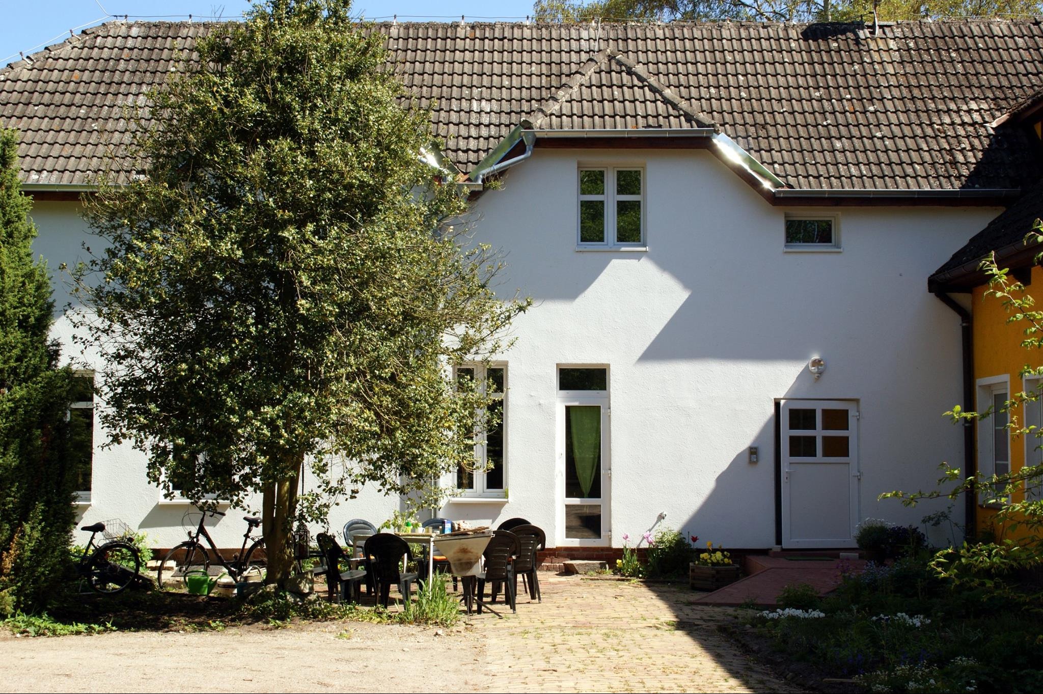 Biały dom jednorodzinny w Szczecinie z oknami i drzwiami, widok z zewnątrz, z brukowanym podjazdem i drzewem na pierwszym planie.