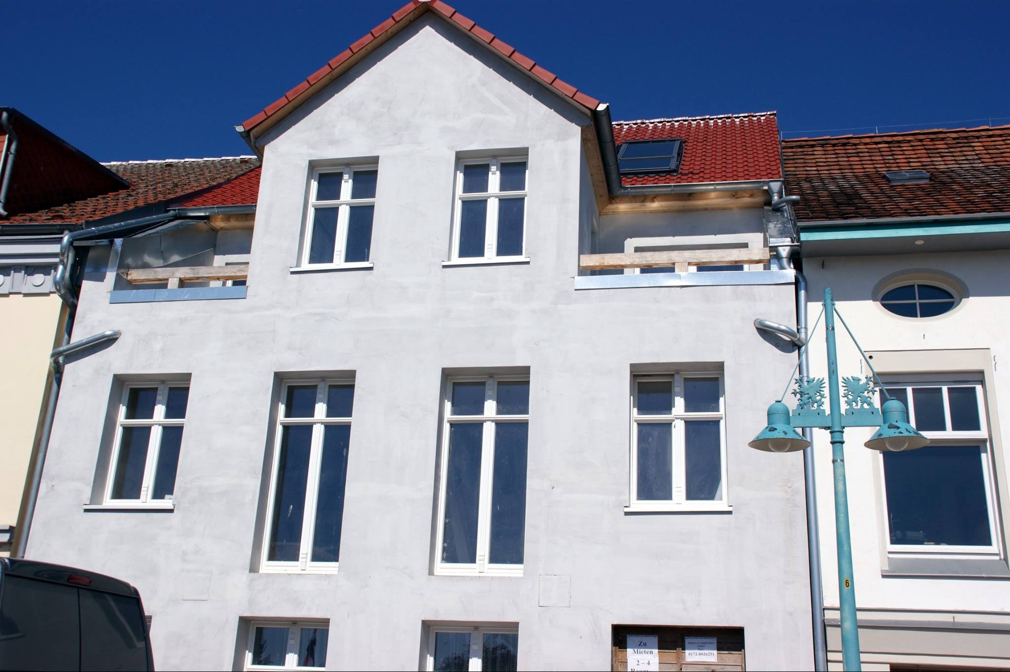 Fasada budynku w trakcie remontu z nowymi oknami i przygotowanym miejscem na okno dachowe, widoczne rusztowania i elementy konstrukcyjne.