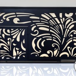 KM Design DOMINIKA KORYCIŃSKA - Czarny panel dekoracyjny z wycinanymi laserowo, kremowymi wzorami roślinnymi, umieszczony na białym, błyszczącym podłożu, z niebieskimi narożnikami ochronnymi i widocznym logo firmy w prawym dolnym...