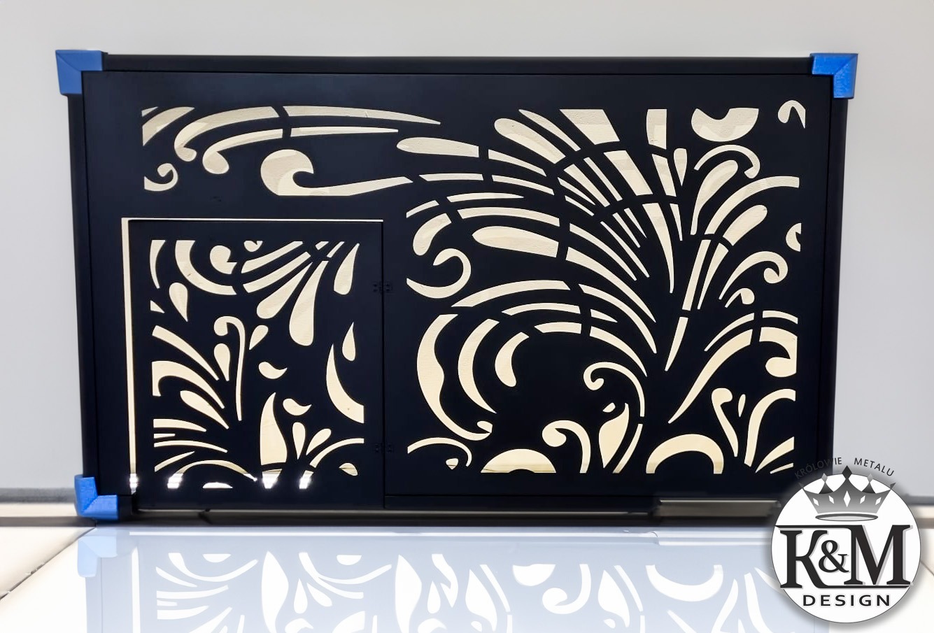 Czarny panel dekoracyjny z wycinanymi laserowo, kremowymi wzorami roślinnymi, umieszczony na białym, błyszczącym podłożu, z niebieskimi narożnikami ochronnymi i widocznym logo firmy w prawym dolnym...