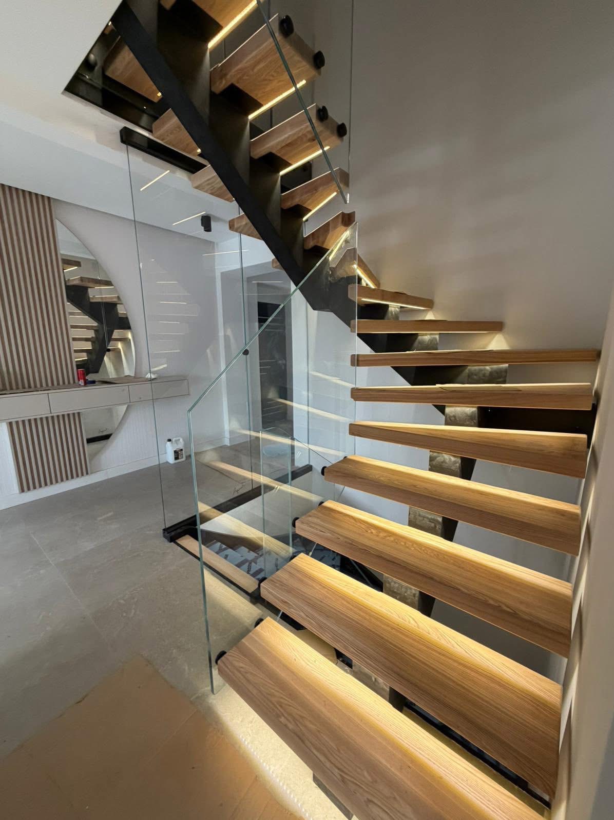 Nowoczesne schody drewniane z podświetleniem LED i szklaną balustradą, widok z dołu, eleganckie wykończenie wnętrza, minimalistyczny design.