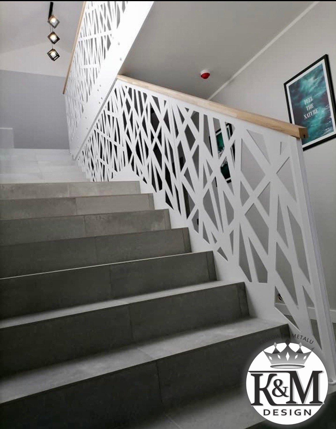 Nowoczesne schody z geometryczną, białą balustradą metalową i drewnianym poręczą. Szare płytki schodowe, minimalistyczny design, oświetlenie punktowe.