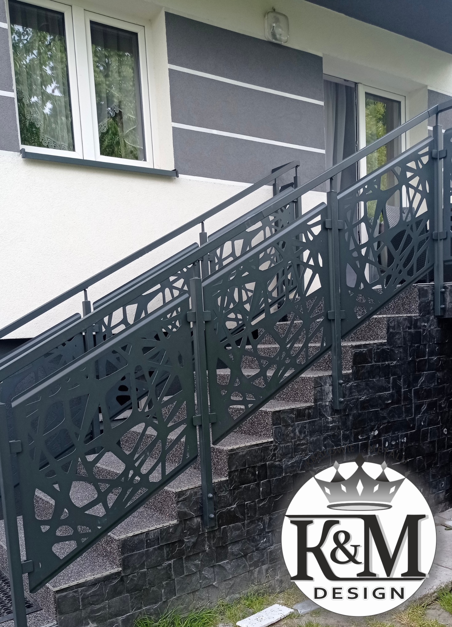 Nowoczesne schody zewnętrzne z metalową balustradą o ażurowym wzorze, prowadzące do budynku z szarą elewacją i białymi oknami. Widoczne logo firmy.