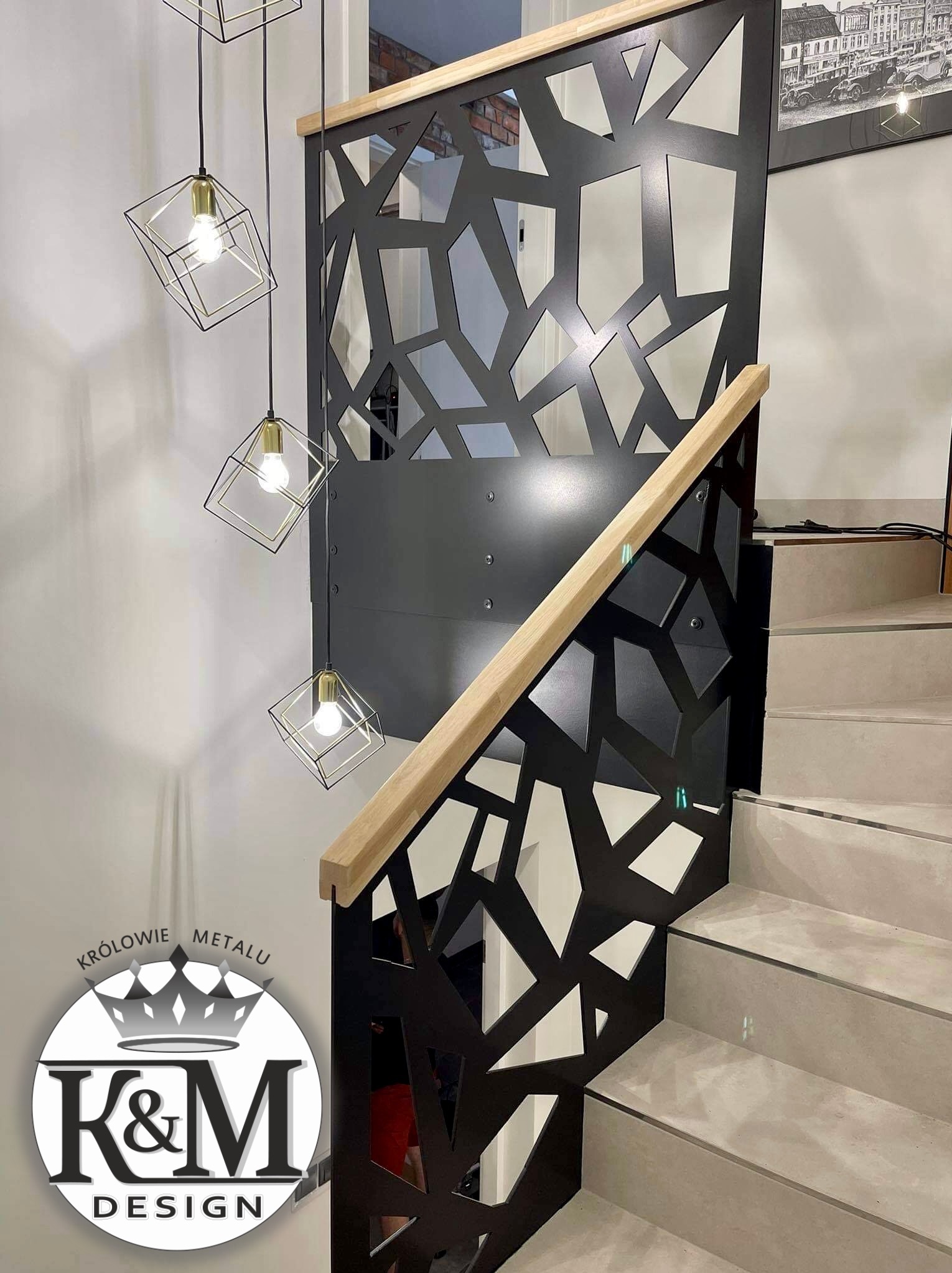 Nowoczesna balustrada schodowa z czarnego metalu o geometrycznym wzorze, drewniany pochwyt, minimalistyczne lampy wiszące, jasne stopnie schodów.