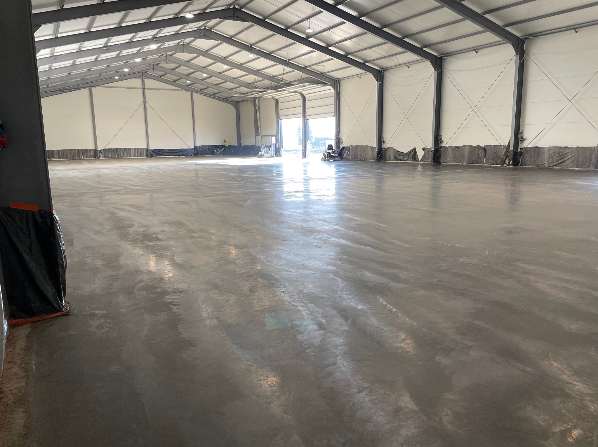 Świeżo wylana, jasnoszara posadzka w dużym, przemysłowym obiekcie w Raszkowie, z widocznymi śladami po maszynach i pracownikach w tle.