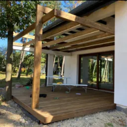 Konstrukcja z belek zadaszenia tarasu drewnianego w trakcie budowy, widoczne narzędzia i materiały budowlane, surowy teren wokół.