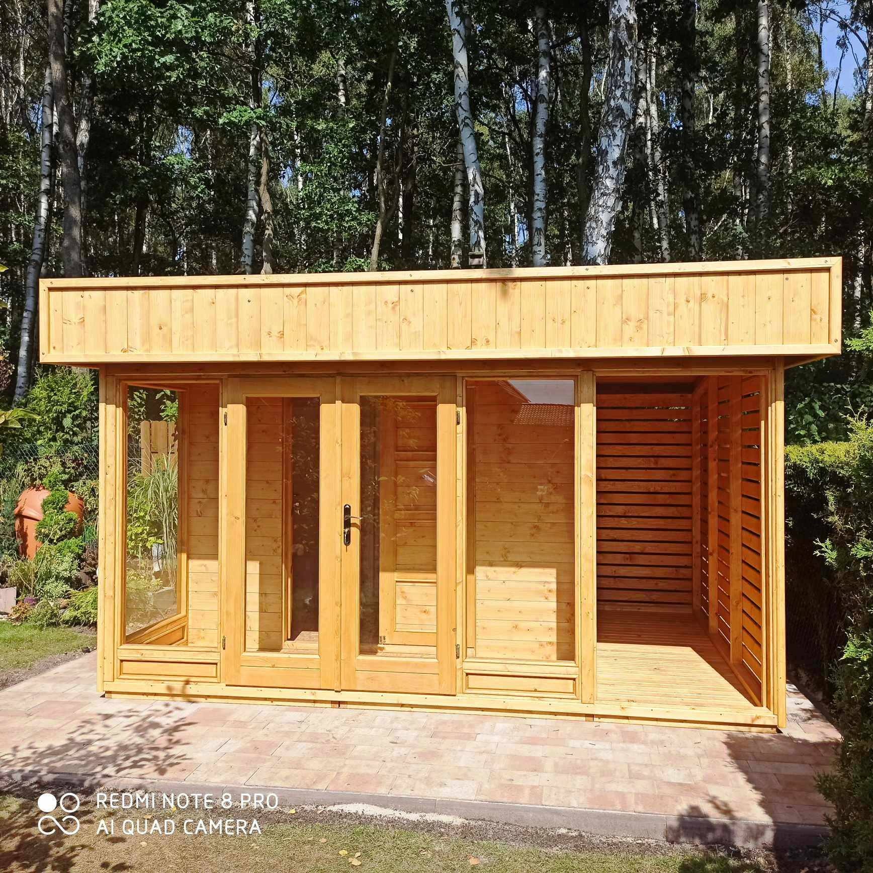 Jasna, drewniana altana z przeszklonymi drzwiami i ażurową ścianą, stojąca na kostce brukowej w otoczeniu drzew i zieleni.