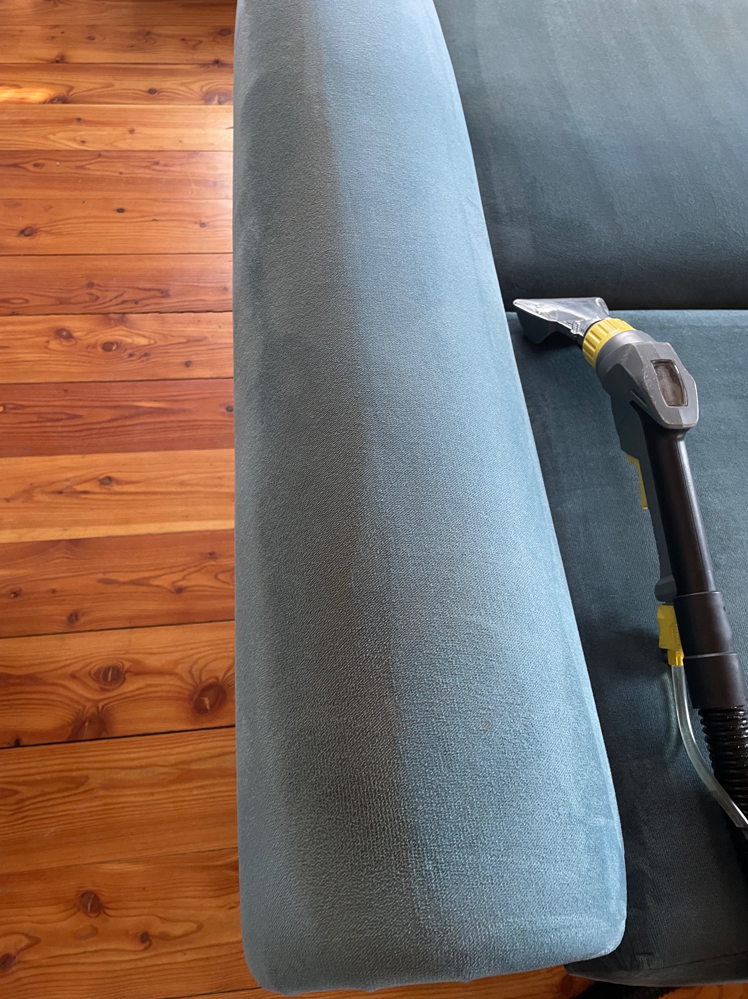 Dysza odkurzacza piorącego na niebieskiej tapicerce kanapy, widoczna drewniana podłoga