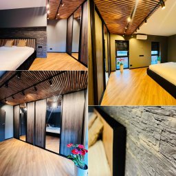 Nowoczesna sypialnia po remoncie: drewniany sufit lamelowy z oświetleniem, kamienna ściana za łóżkiem, podłoga z paneli i szafa z lustrzanymi drzwiami przesuwnymi.