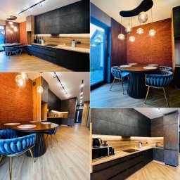 Nowoczesna kuchnia z jadalnią: czarne szafki, drewniane blaty, ceglana ściana, okrągły stół z welurowymi krzesłami i designerskie oświetlenie.