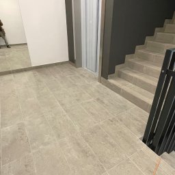 Mykola Vybornyi - Beżowe płytki podłogowe w korytarzu budynku z windą i schodami, widoczny mężczyzna robiący zdjęcie w lustrze.