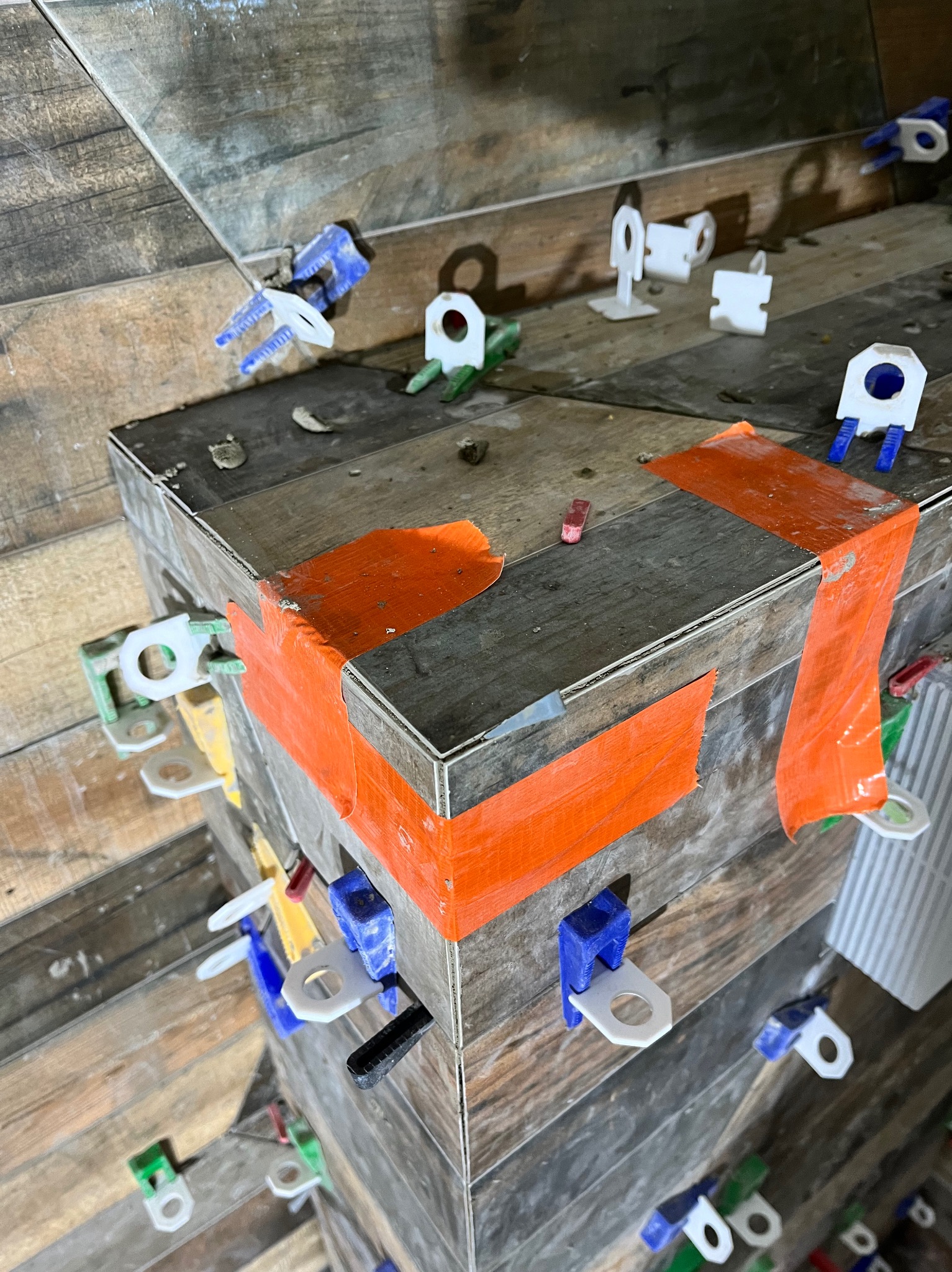 Układanie płytek imitujących drewno z użyciem systemu poziomowania, zabezpieczonych pomarańczową taśmą.