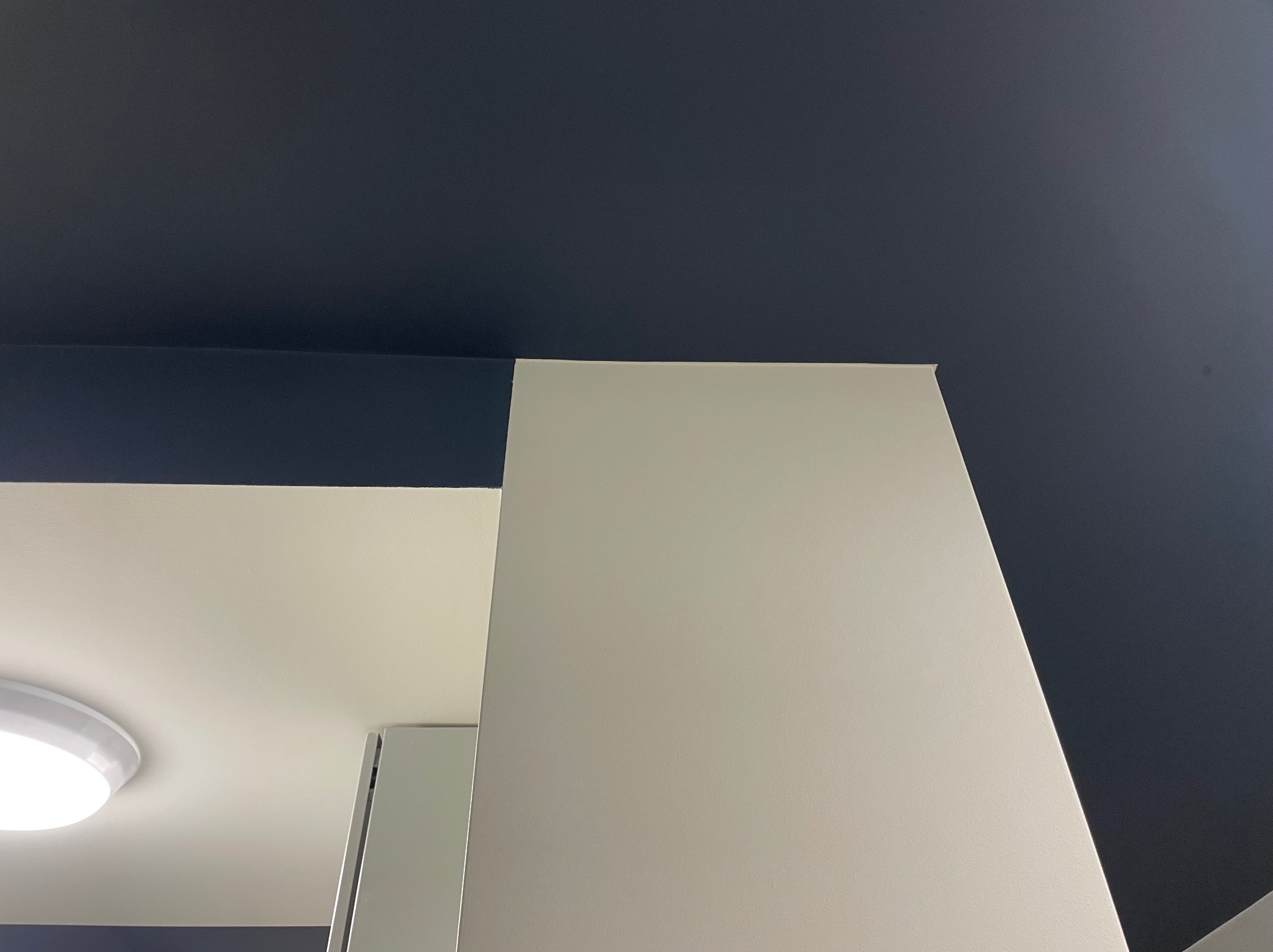 Fragment wnętrza po malowaniu: granatowy sufit kontrastuje z białą ścianą i fragmentem oświetlenia sufitowego.