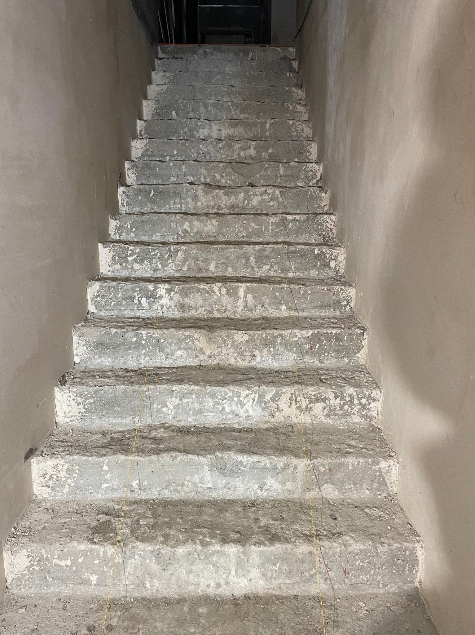 Surowe betonowe schody w trakcie remontu, widoczne ślady po starym wykończeniu i żółta linia pionu.