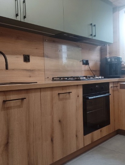 Nowoczesna kuchnia z drewnianymi frontami szafek dolnych i jasnymi szafkami górnymi, czarnymi uchwytami, piekarnikiem i płytą gazową, z ekspressem do kawy na blacie.