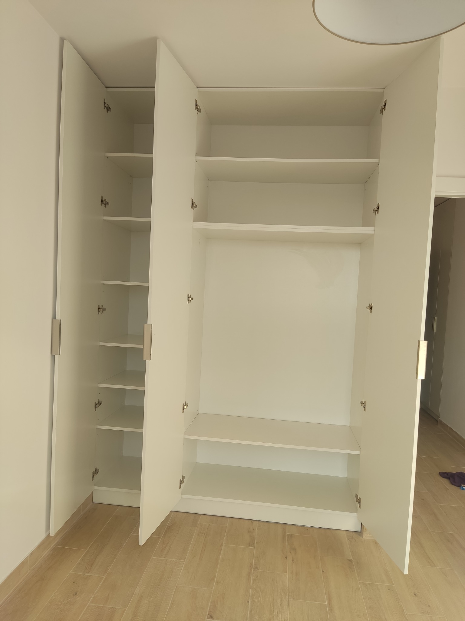 Biała, otwarta szafa wnękowa z półkami i drążkiem na ubrania, widok z przodu, jasne wnętrze, parkiet na podłodze. Minimalistyczny design.