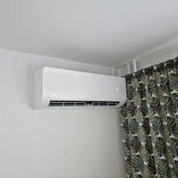 KLASS-INSTAL Szymon Klass - Biały klimatyzator Midea zamontowany na ścianie w pomieszczeniu z zasłoną w liście.