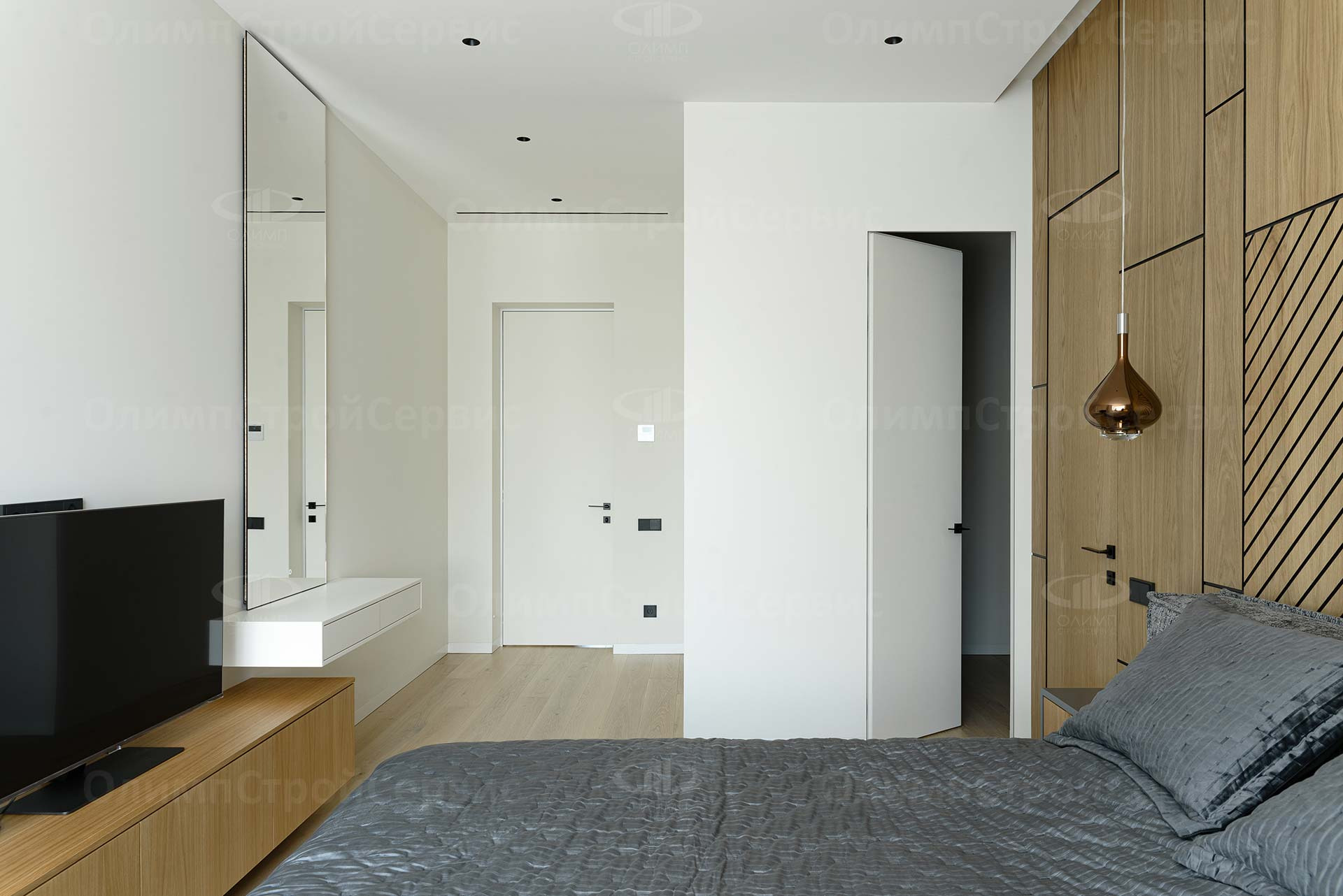 Nowoczesna sypialnia z drewnianą ścianą akcentującą, minimalistycznym oświetleniem i lustrem w pełnej długości, widok na otwarte drzwi do kolejnego pomieszczenia.