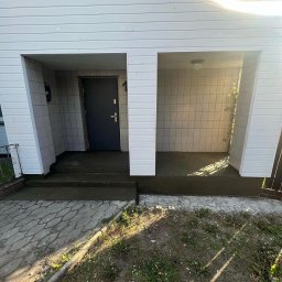 Sowrem - Wykończenia wnętrz Rybnik - Wejście do domu z nowymi, ciemnymi schodami i podłogą w przestrzeni wejściowej, wykończone białymi panelami i płytkami, widok z zewnątrz.