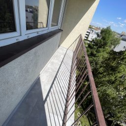 Sowrem - Wykończenia wnętrz Rybnik - Wykończony balkon z szarymi płytkami podłogowymi, brązową balustradą i widokiem na zieleń miejską w słoneczny dzień.
