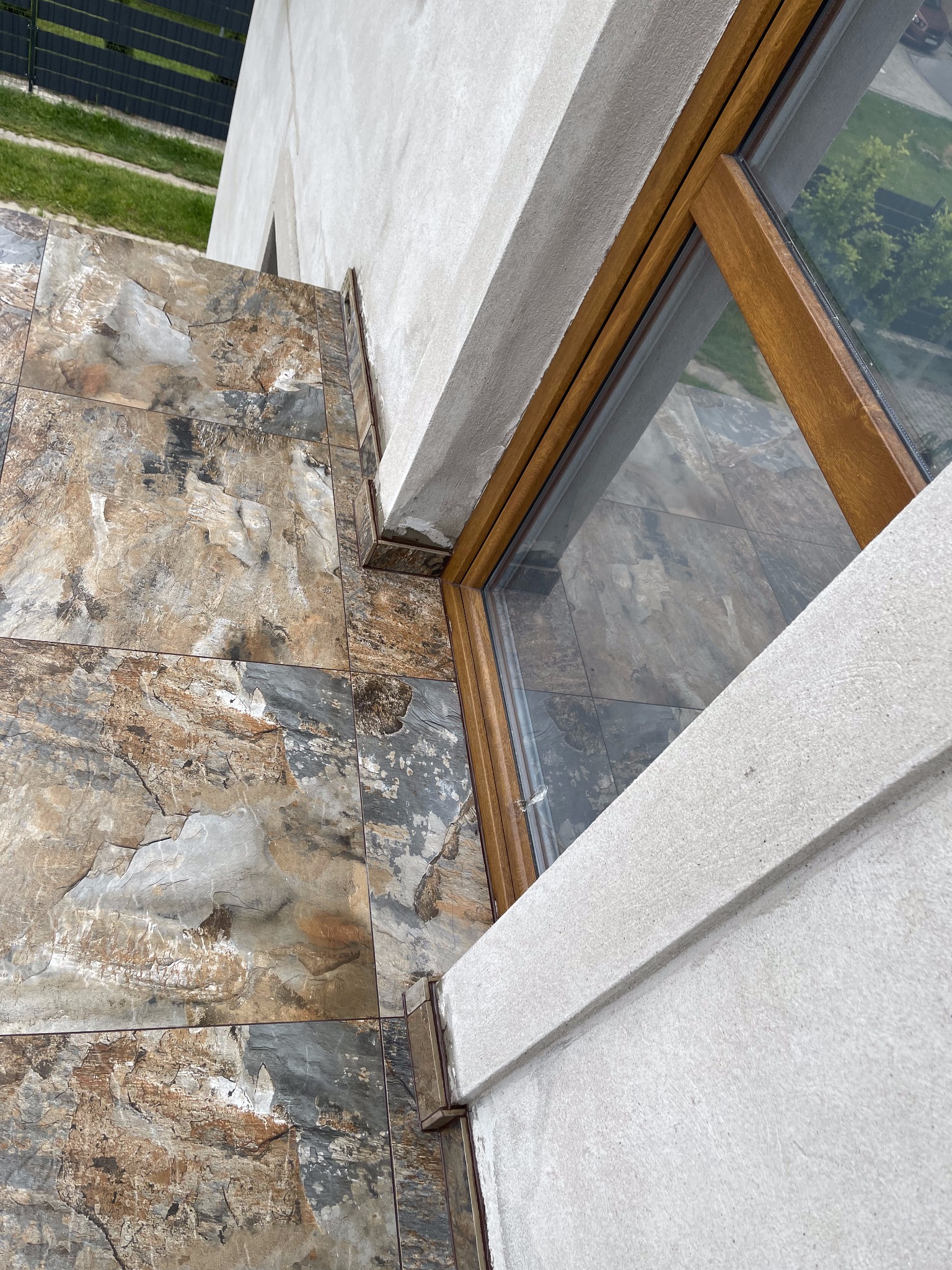 Zewnętrzne płytki podłogowe imitujące kamień, ułożone przy oknie z drewnianą ramą, widok z góry.