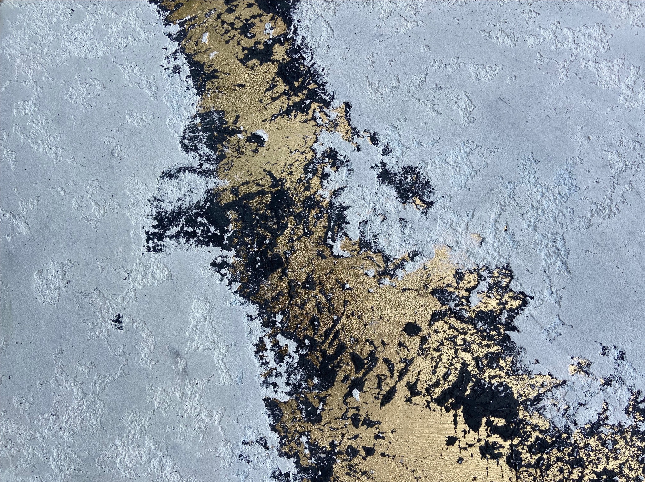 Fragment ściany z dekoracyjnym tynkiem w odcieniach szarości i złota, z wyraźną fakturą i nieregularnymi wzorami.