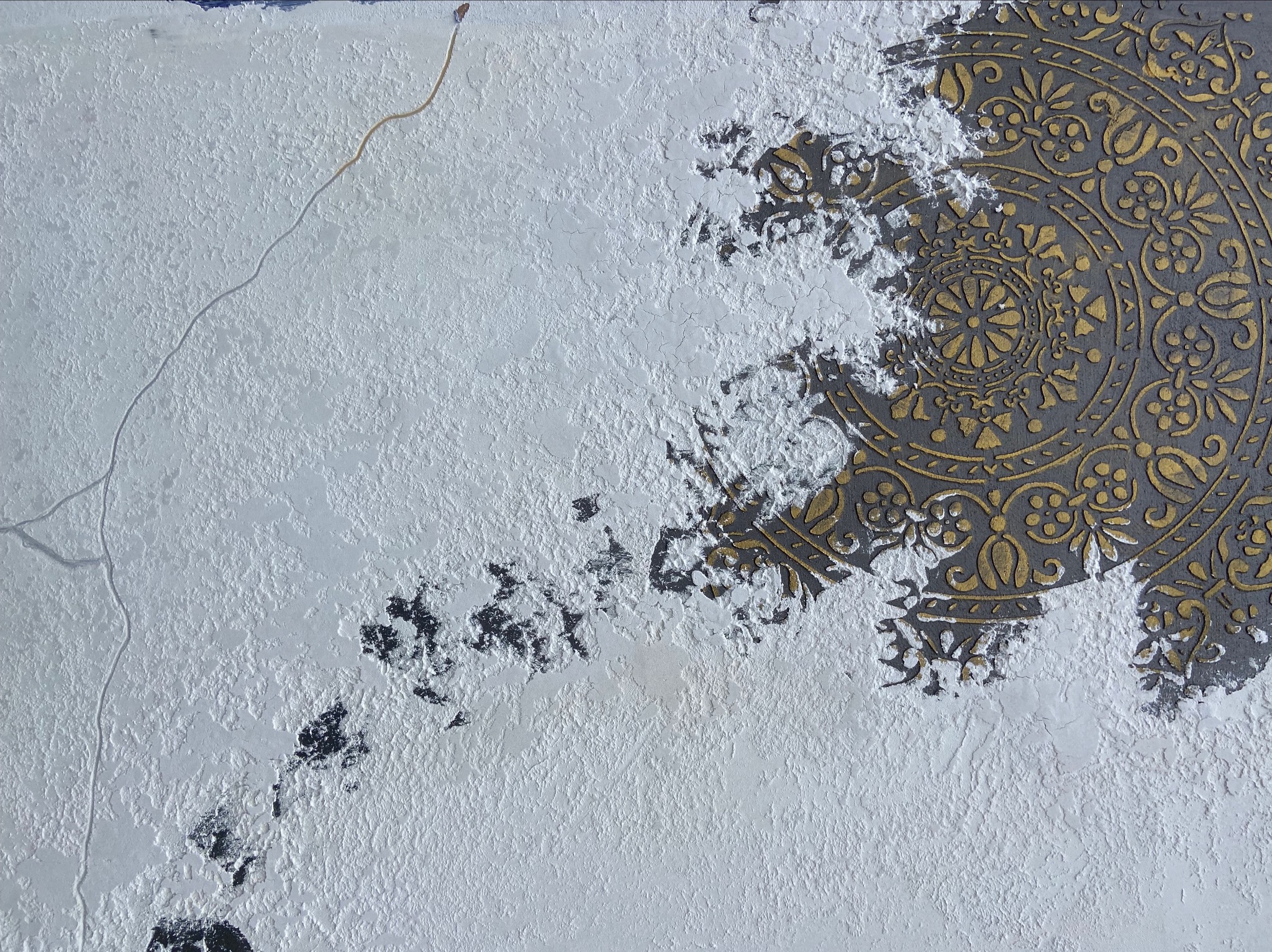 Fragment ściany z dekoracyjnym tynkiem strukturalnym i częściowo odsłoniętym, złoconym wzorem ornamentacyjnym.