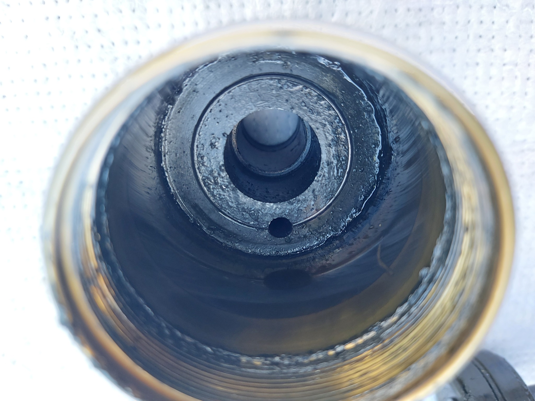 Wnętrze cylindra maszyny z widocznymi śladami zużycia i smaru, sfotografowane z góry, ukazujące metalową konstrukcję z otworem w centrum.