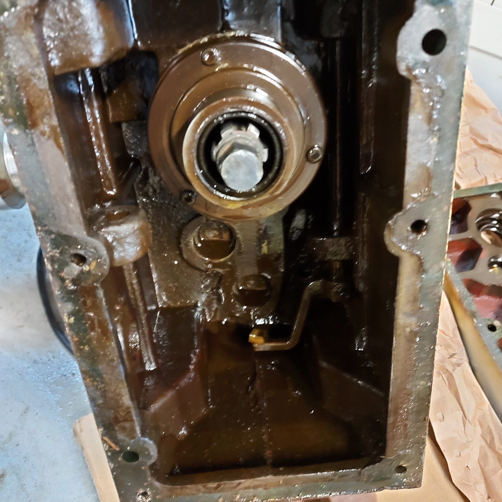 Wnętrze skrzyni biegów maszyny, widoczne elementy przekładni zalane olejem, ślady zużycia i zabrudzenia na metalowych powierzchniach.