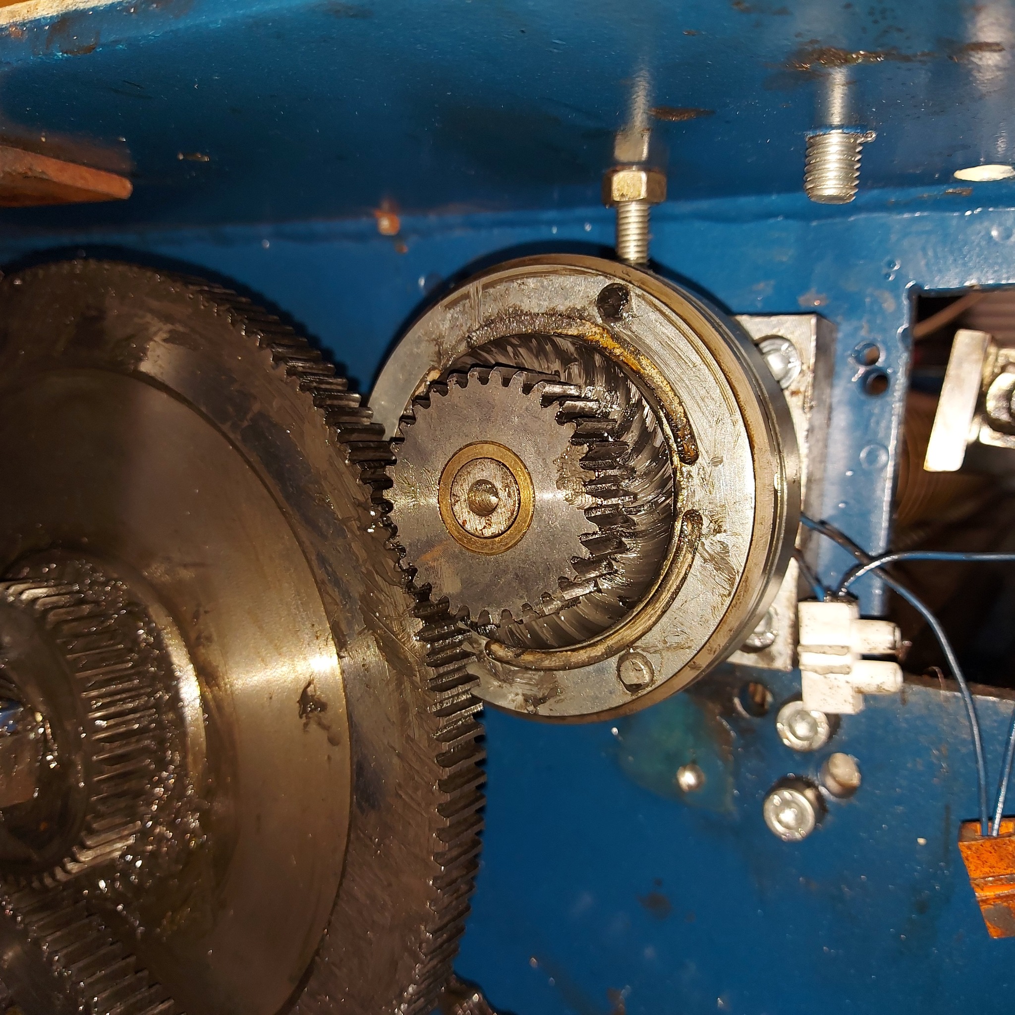 Olej na zębatkach przekładni maszyny w zbliżeniu, widoczne ślady użytkowania i montaż na niebieskiej obudowie.