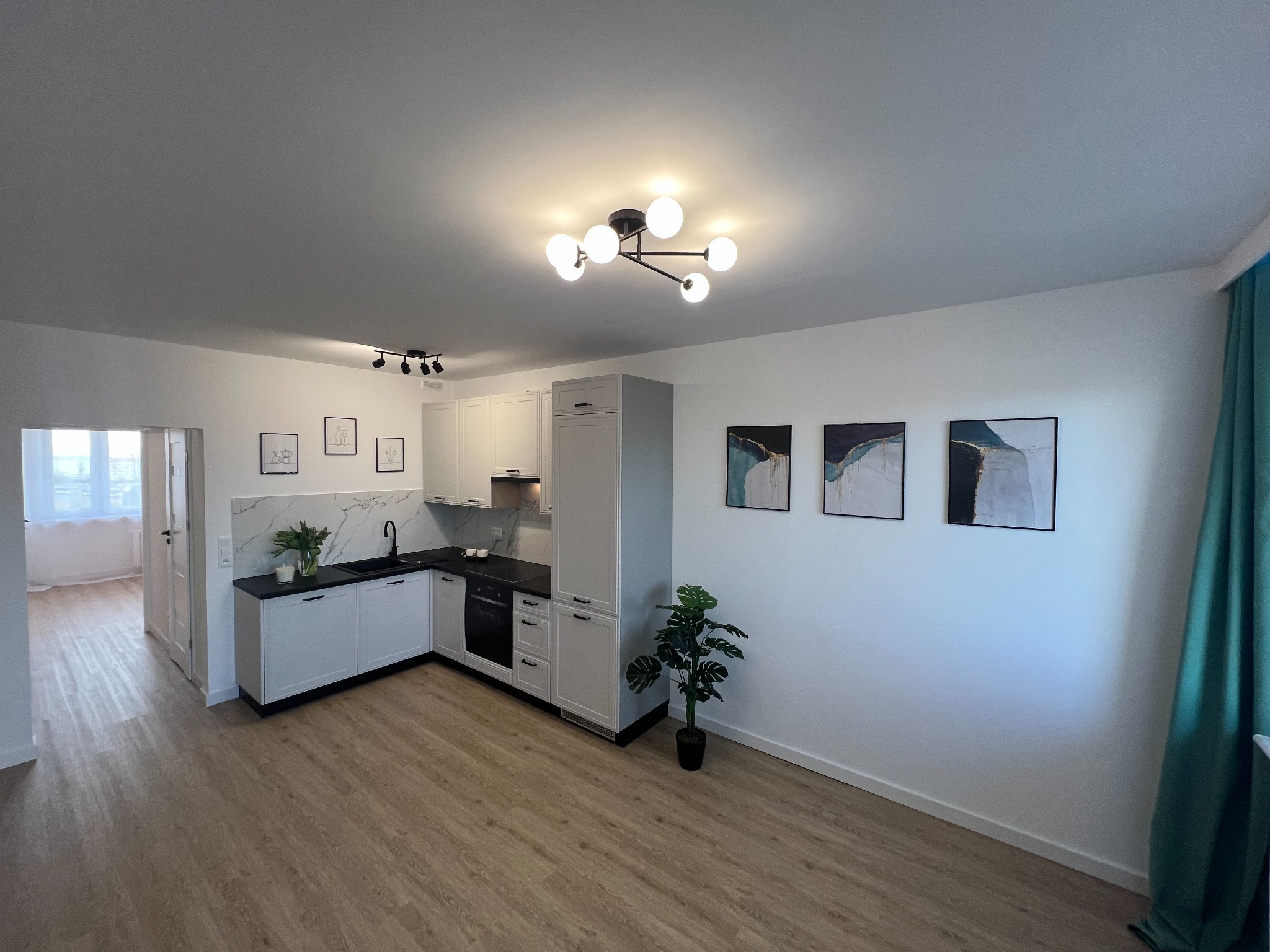 Jasne, przestronne wnętrze po remoncie: kuchnia z białymi szafkami, czarnym blatem i marmurowym backsplashiem, drewnopodobna podłoga, nowoczesne oświetlenie sufitowe i minimalistyczne obrazy...