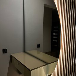 WOOD DESIGN Hubert Śmiglewski - Nowoczesna toaletka z szufladą i okrągłym lustrem z podświetleniem LED, zamontowana na szarej ścianie, obok drewnianej ściany z pionowych listew.