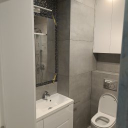 F.U.H. SZYMON REMONTUJE - Nowoczesna łazienka z szarymi płytkami, białą umywalką z szafką, toaletą i lustrem z mozaiką, oświetlona punktowo.