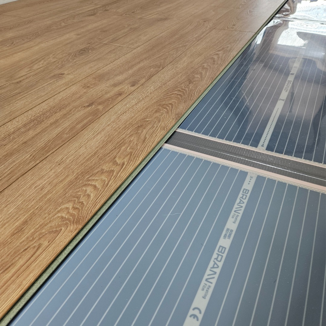 Montaż podłogowej folii grzewczej BRAVAV pod panele podłogowe, widoczne połączenia i białe linie grzewcze.