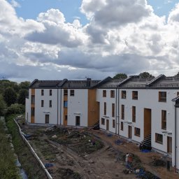 Usługi Transportowe Józef Basarab - Nowoczesne, białe domy szeregowe z panelami słonecznymi na dachu, widoczne z góry, z przygotowanym terenem pod ogródki i instalacjami na zewnątrz.