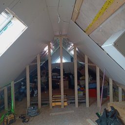 D&P-BUD Łapiński Patryk - Poddasze w trakcie adaptacji: drewniana konstrukcja szkieletowa, częściowo zamontowane płyty gipsowo-kartonowe, widoczne narzędzia budowlane i laser krzyżowy wyznaczający poziom, w tle zgromadzone...