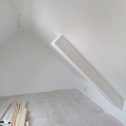 D&P-BUD Łapiński Patryk - Poddasze w trakcie prac wykończeniowych, widoczne drewniane listwy przypodłogowe, przewody elektryczne wystające ze ściany oraz świeżo pomalowane ściany na biało.