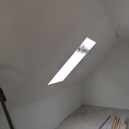 D&P-BUD Łapiński Patryk - Poddasze po malowaniu na biało, widoczne okno dachowe, drabina oparta o ścianę, na podłodze szczotka, listwy przypodłogowe i inne narzędzia.