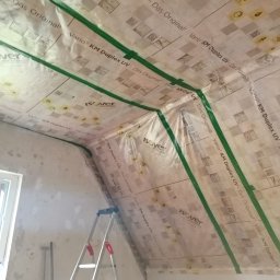 D&P-BUD Łapiński Patryk - Poddasze w trakcie ocieplania, widoczna folia paroizolacyjna Isover Vario KM Duplex UV z zielonymi taśmami uszczelniającymi na krokwiach, drabina oparta o ścianę, surowy stan ścian.