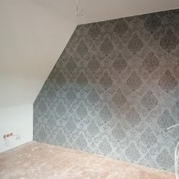 D&P-BUD Łapiński Patryk - Pokój na poddaszu z nową tapetą w odcieniach szarości o klasycznym wzorze, widoczne gniazdka elektryczne i wystające kable, podłoga w trakcie przygotowania.
