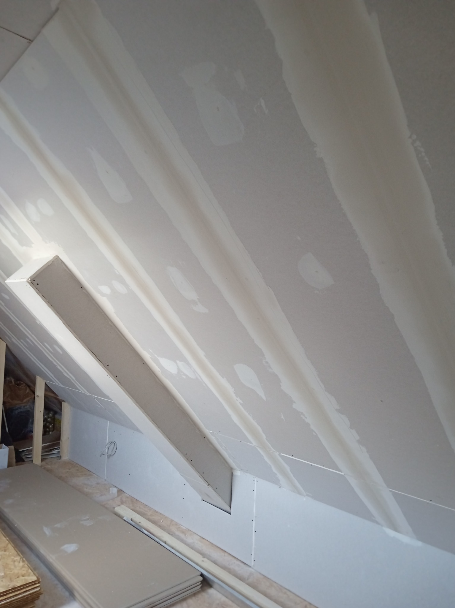 Skośny sufit poddasza z zamontowanymi płytami karton-gips, widoczne łączenia zaszpachlowane, fragmenty płyt leżą na podłodze.