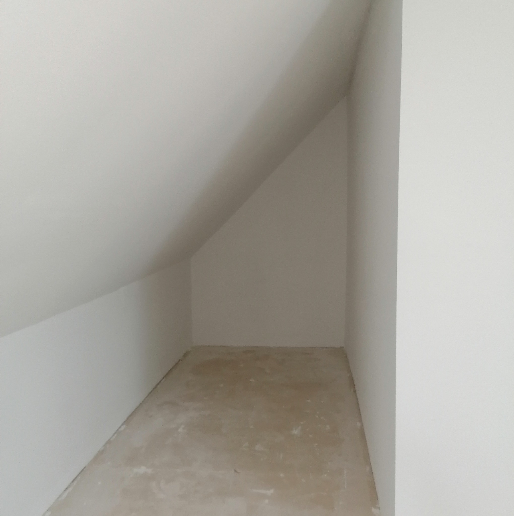 Poddasze z widoczną skośną ścianą, przygotowane do ocieplenia, surowy beton na podłodze.