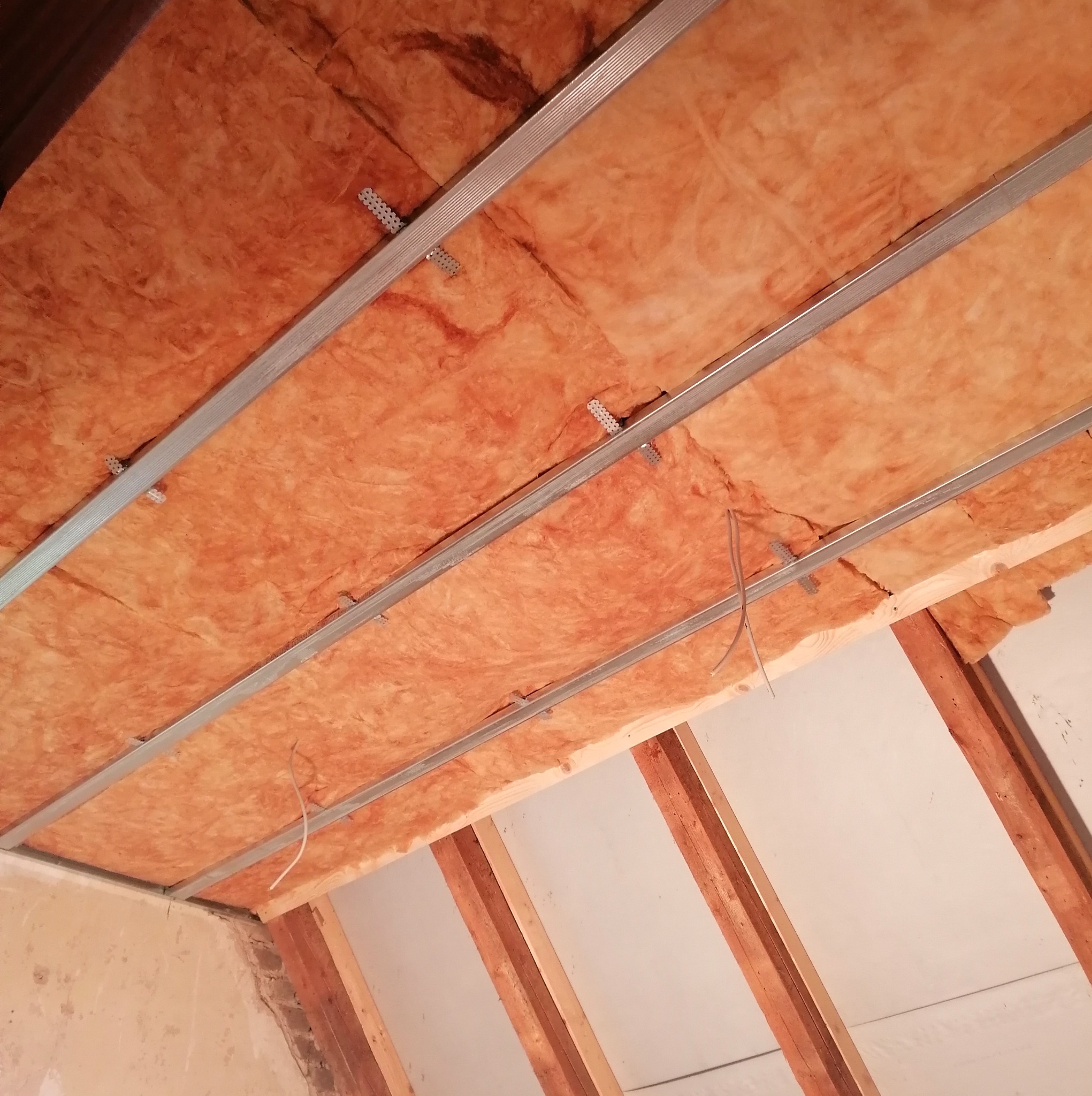 Poddasze w trakcie ocieplania wełną mineralną, widoczne metalowe profile montażowe i drewniana konstrukcja dachu.