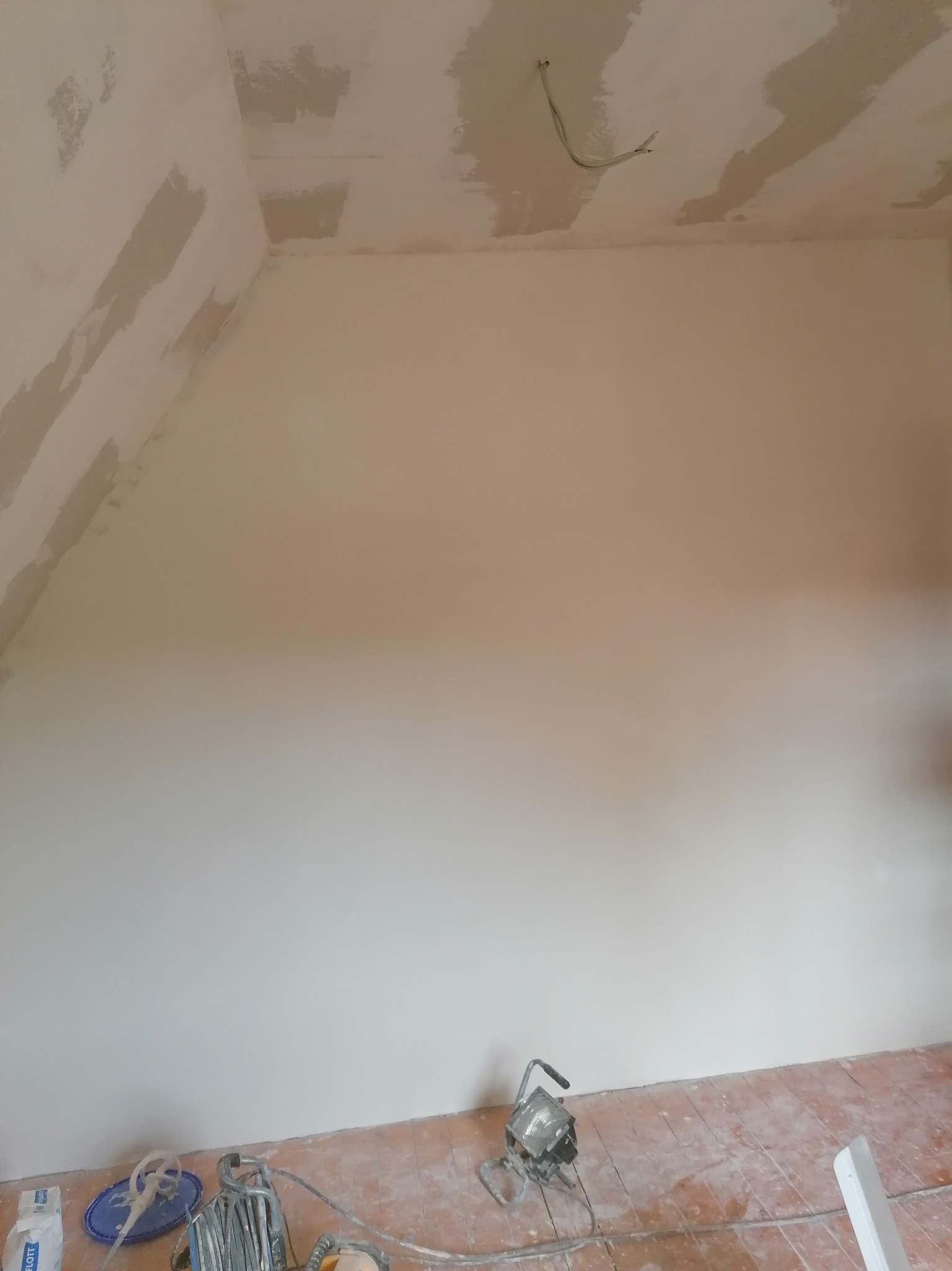 Ściana po szpachlowaniu z widocznymi śladami łączeń płyt karton gips, przygotowana do malowania, z narzędziami i workiem gładzi na podłodze.